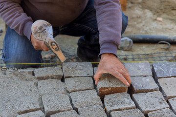 Canvas Print - Road worker using stones and hammer to build stone road of construction laying stones