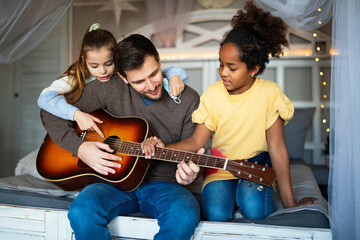 Wall Mural - Smiling father with multiethnic children having fun and playing guitar at home