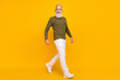 Photo of positive traveler old man walk wear glasses green shirt pants sneakers isolated yellow color background