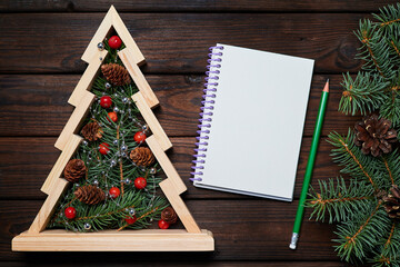 Wall Mural - Wooden christmas tree with Fir branches inside and a Blank notepad on wooden background