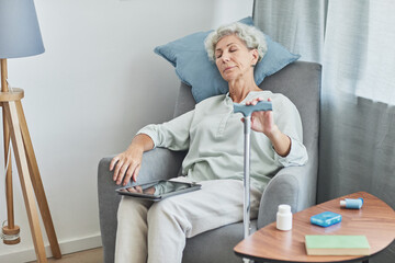 Portrait of white haired senior woman sleeping in comfortable armchair at home with cane, copy space