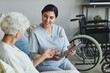 © Seventyfour - Smiling female nurse using digital tablet while surveying senior woman in retirement home, copy space