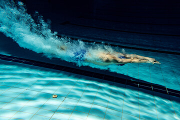 Wall Mural - Underwater camera work. One male swimmer training at pool, indoors. Underwater view of swimming movements details.