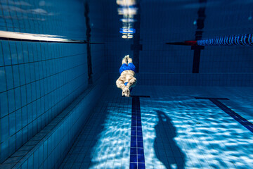 Wall Mural - Underwater shooting. One male swimmer training at pool, indoors. Underwater view of swimming movements details.