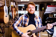 Man With Red Ginger Hair And Beatd Is Considering A Guitars In A Music Store