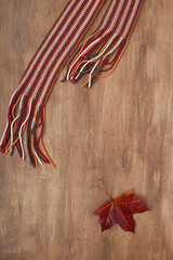 Autumn red maple leaf and scarf on wooden background