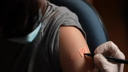 closeup suggestive shot of a doctor drawing a red heart on the patch of a boy with a surgical face m