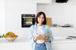 © Prostock-studio - Young lady smiling and taking notes, holding notepad and pen, standing in kitchen interior, planning her day
