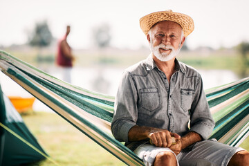 Wall Mural - portrait of happy mature man relaxes in hammock while camping and looking at camera.