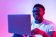 © Prostock-studio - Happy young black man using laptop computer for online work, education or communication in neon light