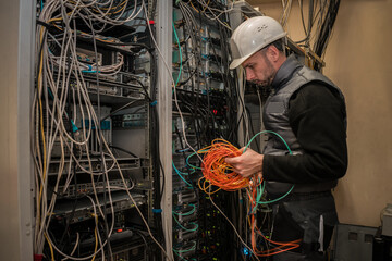 An engineer in a white helmet works in a server room. Technician connects fiber optic cables with network interfaces in the data center