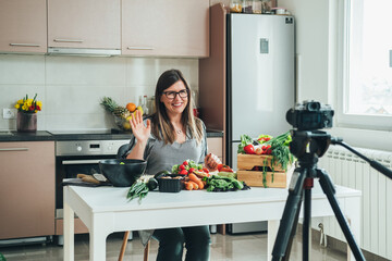 Smiling Woman Recording Video Tutorial Session of Online Cooking Lesson at Home. 
Happy female chef waving and saying hello or goodbye while filming a video tutorial for her youtube food channel.