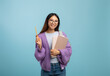 © Prostock-studio - I know the answer. Excited asian female student in eyeglasses holding notepad and pointing pencil up, blue background