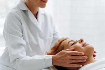 Cropped view of the masseuse hands massaging face of charming lady at spa salon. Woman laying at the couch and receiving spa procedures