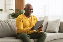 Mature African American Man Using Digital Tablet Sitting At Home