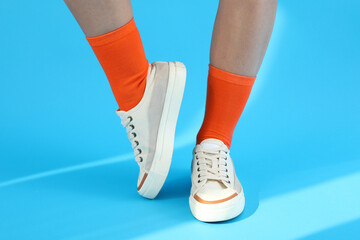 Canvas Print - Female legs in orange socks and sneakers on blue background