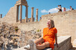 Black Hipster traveler smiling sitting in ruins, on the background of the Parthenon on the Acropolis of Athens, Greece. Vacation woman enjoying the visit in Athens
