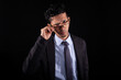 Businessman taking off glasses and looking suspiciously, isolated on black background. A young adult latin man frowns with a distrustful look