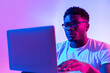 © Prostock-studio - Focused young black man in glasses using laptop computer for online work or communication in neon light