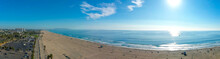A Stunning Aerial Panoramic Shot Of The Coastline With Vast Blue Ocean Water, Waves Rolling In, Silky Sand And The Cityscape Along The Beach With Blue Sky And Clouds At Santa Monica Beach