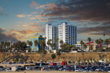 A Gorgeous Shot Of Beach Front Hotels With Lush Green Palm Trees And Parked Cars Near A Sandy Beach With Powerful Clouds And Sunset At Santa Monica Beach In California USA