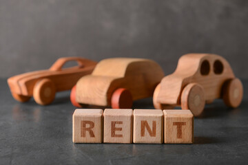 Wall Mural - Word RENT with wooden cars on dark background, closeup