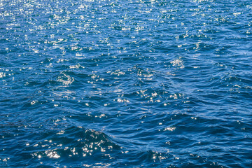 Blue sea waves in sunshine glow as surface background. Summer holidays and coastal nature concept