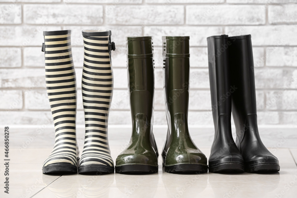Different rubber boots on floor near brick wall