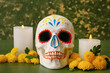 Painted human skull for Mexico's Day of the Dead (El Dia de Muertos), candles and flowers on green wooden background