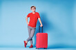 Travel concept. Full length colorful studio portrait of young man in hat with valise on blue background.