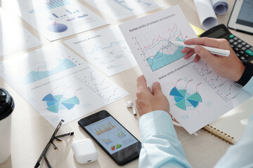 Hands of business person pointing at area chart in his hands when analyzing activity of his business