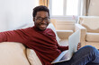 © Dragana Gordic - Portrait of smiling African American man in glasses sit at sofa in office working on laptop, happy biracial male worker look at camera posing, busy using modern computer gadget at workplace