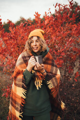 Wall Mural - Young woman drinking hot tea from thermos in beautiful autumn forest.