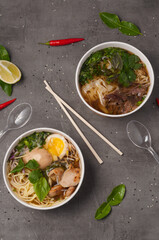 a still life of Asian ramen soups and a photo on a gray background in craft dishes. concept: food delivery, street food