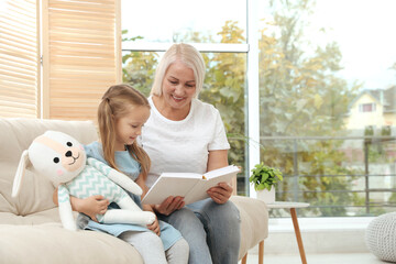 Wall Mural - Happy grandmother with her granddaughter reading book together at home