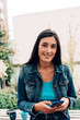 © Carlo - casual smiling young caucasian woman with long black hair wearing jeans and holding a mobile phone while looking at camera