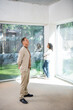 © LIGHTFIELD STUDIOS - man looking at ceiling near african american wife standing near panoramic windows in new house