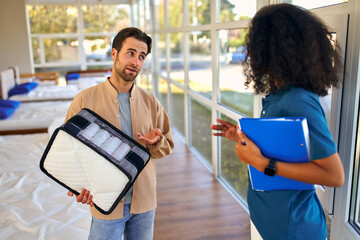 Wall Mural - An African American female salesperson consultant advises a man who is holding a mattress sample in a bed, mattress and pillow store.