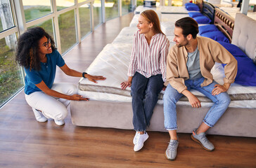 Wall Mural - African American saleswoman helps customers choose an orthopedic mattress in a store. A young couple is buying a mattress and bed and various bedding accessories.