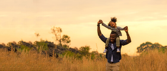 Happy African family child daughter riding the neck father and running on meadow nature on silhouette lights sunset.  Travel and Family Concept, copy space for banner