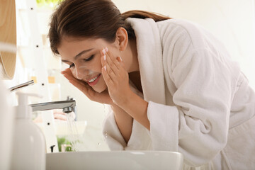 Poster - Beautiful teenage girl washing face with cleansing foam in bathroom. Skin care cosmetic