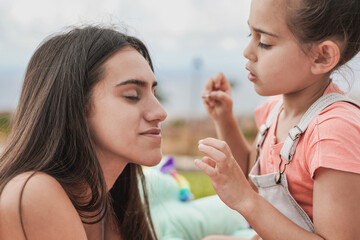 Wall Mural - Cute little girl making up her big sister with glitter eye shadow at home outdoor in the garden