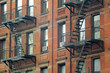 Gritty exterior of orange brick  tenement style apartment building with black fire escapes in central Manhattan, New York City