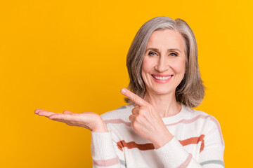 Sticker - Photo of adorable shiny lady pensioner wear striped pullover pointing finger holding arm empty space isolated yellow color background