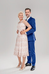 Fashionable elegant couple. Man in suit and woman in evening gown standing embraced, smiling and looking at the camera.