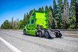 Bright green powerful big rig semi truck tractor without the semi trailer running on the wide highway road to warehouse for pick up next freight load