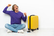 © luismolinero - Young blonde man with suitcase sitting on the floor celebrating a victory