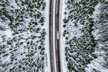 Wall Mural - Aerial view of snow covered road in winter forest white truck driving by road seen from the air. Top view landscape. shooting from a drone. Cargo delivery in winter