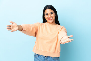 Wall Mural - Young latin woman woman isolated on blue background presenting and inviting to come with hand