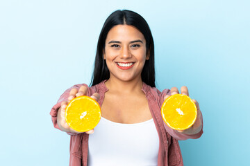 Wall Mural - Young latin woman woman isolated on blue background holding an orange